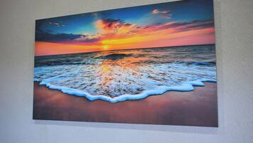 Un tableau représentant un coucher de soleil sur l’océan, avec des vagues sur la plage.
