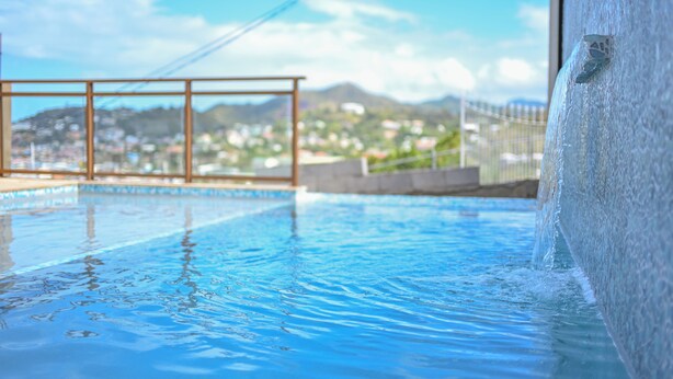En swimmingpool med klart vatten, ett metallräcke och en utsikt över ett kuperat landskap i bakgrunden.