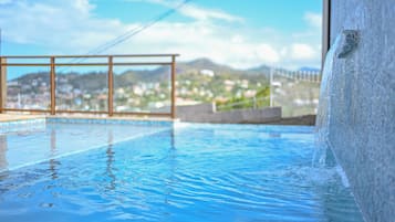 A swimming pool with clear water, a metal railing, and a view of a hilly landscape in the background.