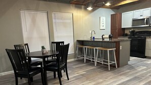 A dining area with a table and chairs, a kitchen with modern appliances, and a bar stool area.