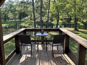 A wooden deck with two wicker chairs and a small round table, overlooking a pond and trees.
