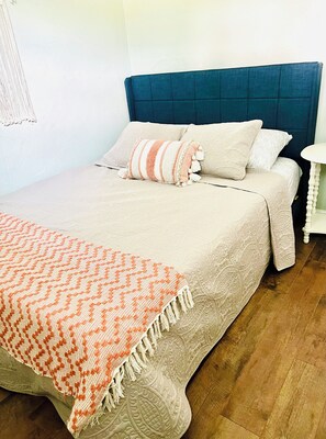 A neatly made bed with a striped pillow and a patterned blanket, a blue headboard, and a small bedside table. - The Riesling Ranch - Wine Trail, Vineyards, Breweries, Hiking (Hector)