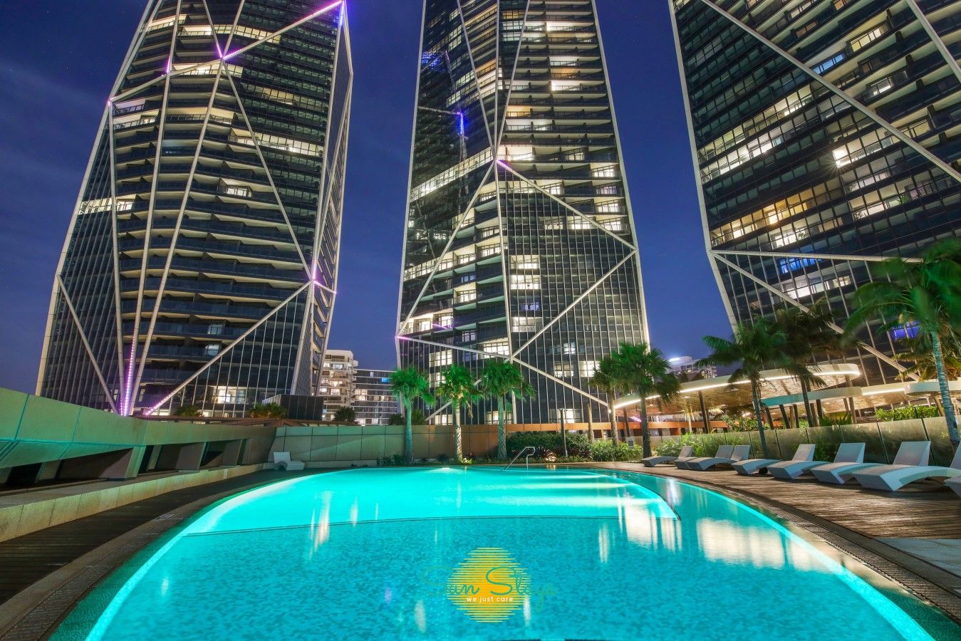 A modern hotel with a pool, surrounded by tall buildings and palm trees.