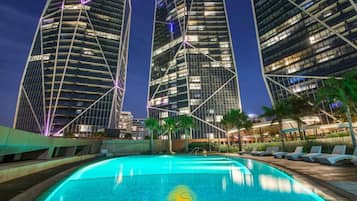A modern hotel with a pool, surrounded by tall buildings and palm trees.
