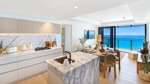 A modern kitchen with marble countertops, a dining area with a view of the ocean, and a cozy seating area with a large window. - Infinity Oceanview 2 Bedroom Suite - The Langham (Surfers Paradise)