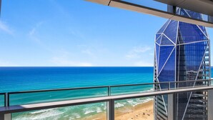 A view of a beach with a clear blue ocean and a modern building with a glass facade. - Infinity Oceanview 2 Bedroom Suite - The Langham (Surfers Paradise)