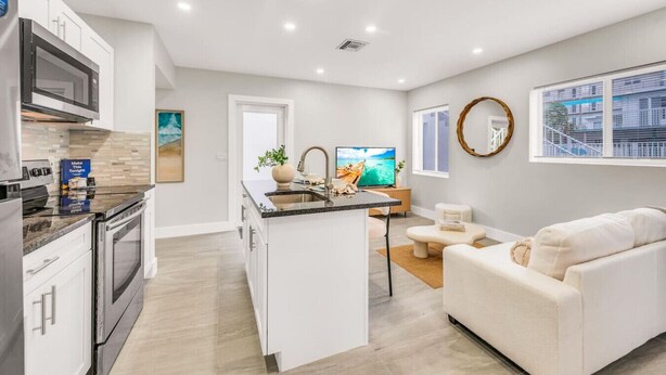 A modern kitchen with a central island, a dining area with a TV, and a living room with a sofa. - The Loggerhead | Private 3-Unit Oceanview Retreat (Fort Lauderdale)