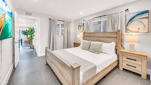 A modern bedroom with a wooden bed, a nightstand, a lamp, and a large abstract painting on the wall. - The Loggerhead | Private 3-Unit Oceanview Retreat (Fort Lauderdale)
