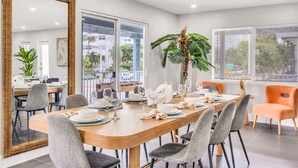A dining area with a large wooden table set for six, surrounded by grey upholstered chairs. A large mirror and a potted plant are visible in the background. - The Loggerhead | Private 3-Unit Oceanview Retreat (Fort Lauderdale)