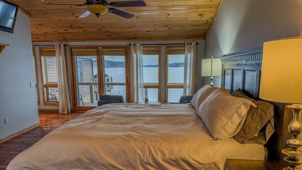 Ein Schlafzimmer mit einem großen Bett, einem Deckenventilator und Blick auf einen See durch große Fenster.