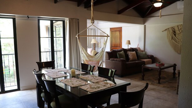 A dining area with a table set for four, surrounded by chairs. There is a hanging chair in the center. - Beautiful 2-bedroom condo with AC in Tamarindo (Tamarindo)