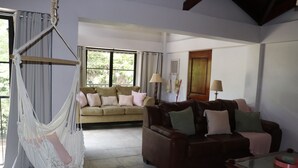 A living room with a hammock, a brown leather sofa, a beige sofa, and a glass coffee table. - Beautiful 2-bedroom condo with AC in Tamarindo (Tamarindo)