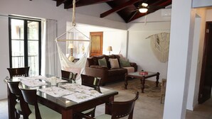 A dining area with a glass table, wooden chairs, and a hanging chair. There is a sofa and a coffee table in the background. - Beautiful 2-bedroom condo with AC in Tamarindo (Tamarindo)