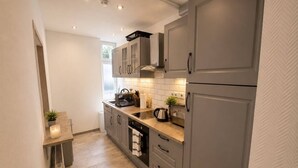 A modern kitchen with grey cabinets, a countertop with a kettle, and a window providing natural light.