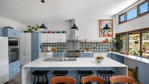 A modern kitchen with a central island, bar stools, and a dining table. - Hyams Reach Retreat - Jervis Bay stay, pets welcome (Shoalhaven City Council)
