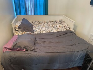 Ein Bett mit einem blumengemusterten Kopfteil, einer grauen Decke und einem rosafarbenen Kissen.