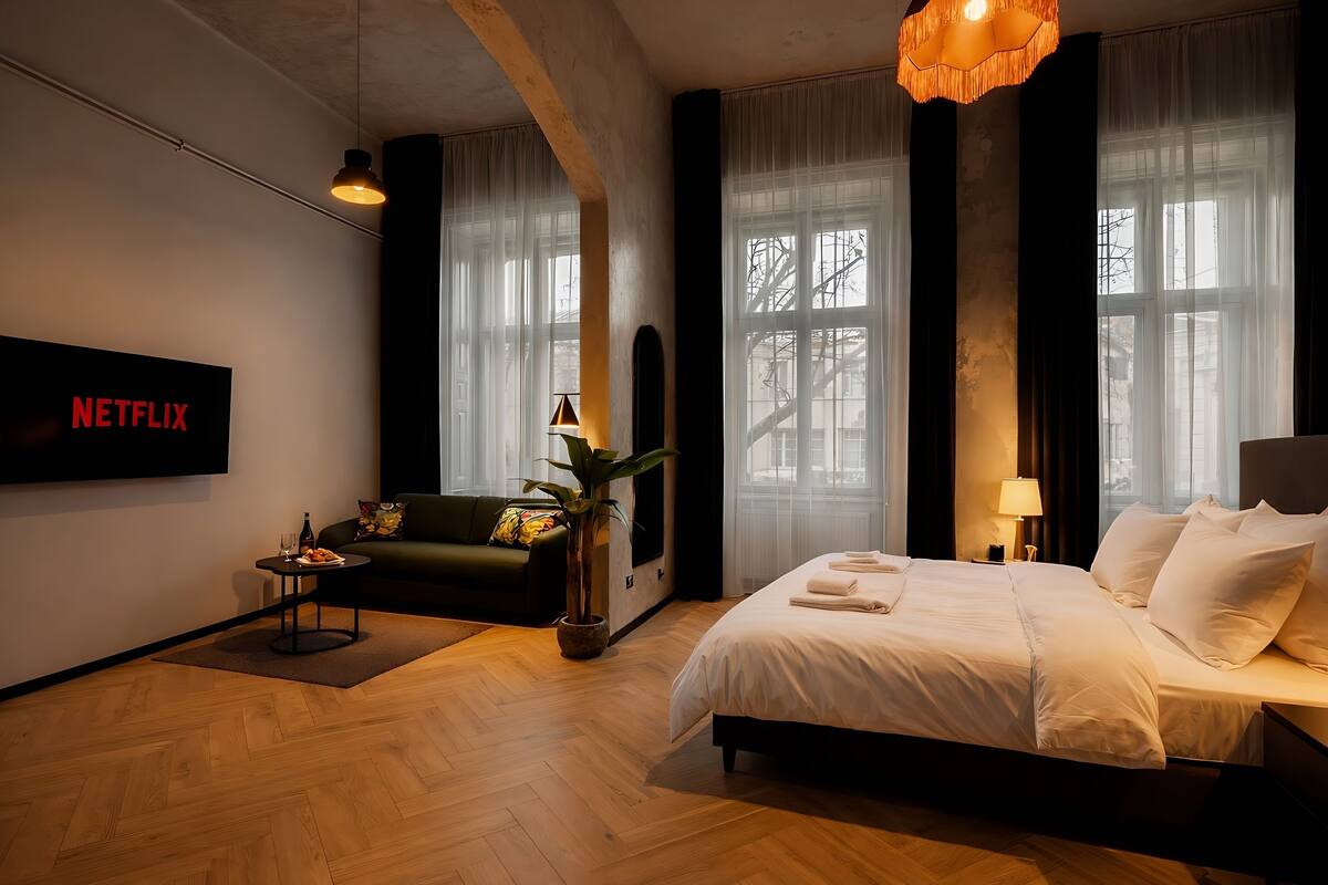 Une chambre d’hôtel moderne avec un grand lit, un canapé, une petite table avec une plante et un téléviseur fixé au mur qui affiche « NETFLIX ».