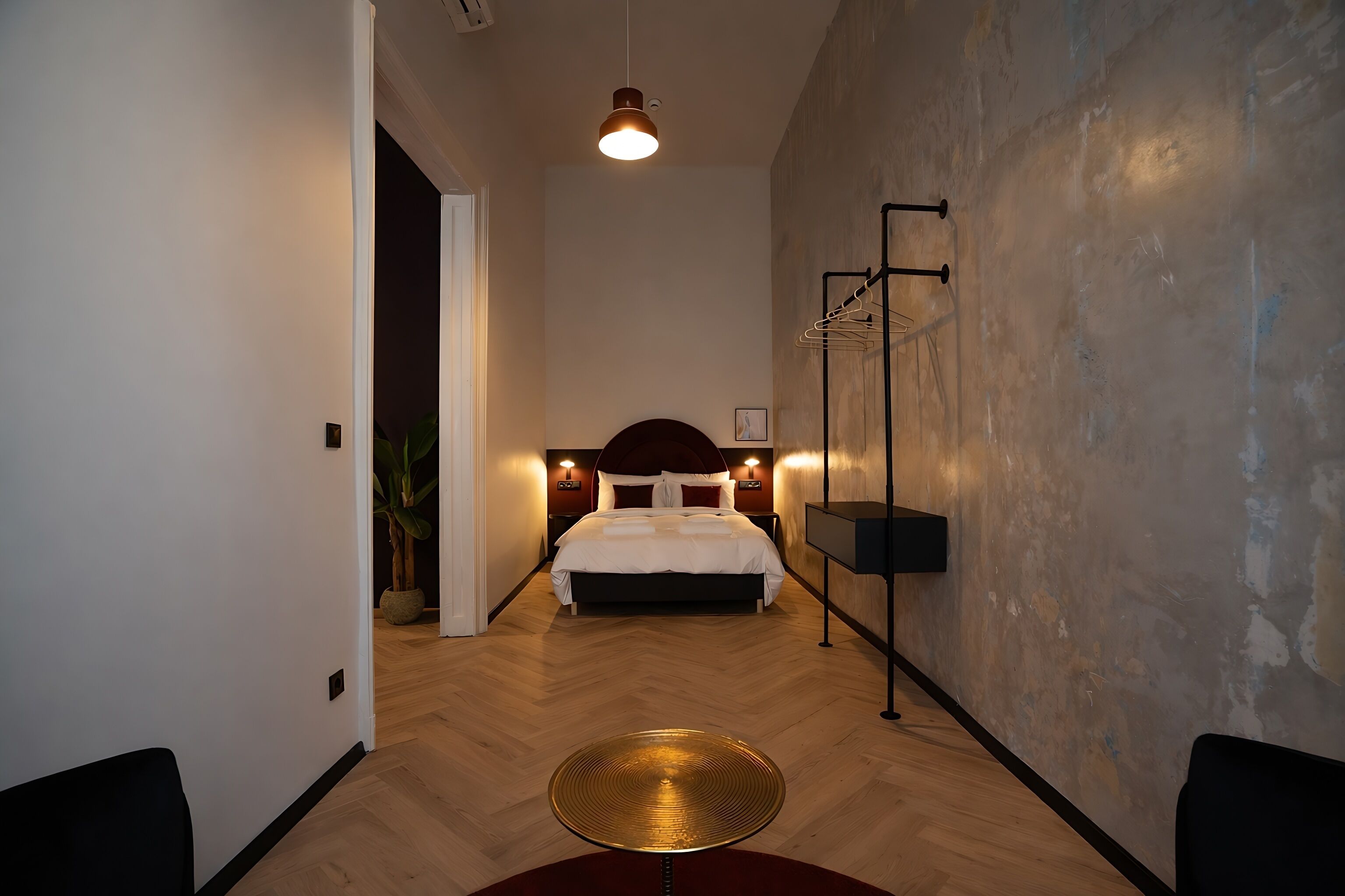 Una habitación de hotel moderna con una cama grande, una mesa redonda y un perchero en la pared.