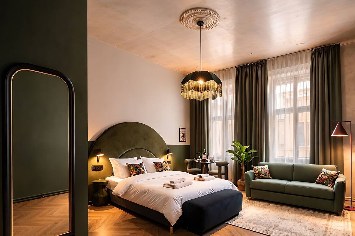 Une chambre moderne avec un grand lit, un canapé vert, un miroir et un lustre.