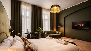 A modern hotel room with a large bed, a sofa, a TV displaying the Netflix logo, and a large window with curtains. - Maroon & Moss Residence (Budapest)