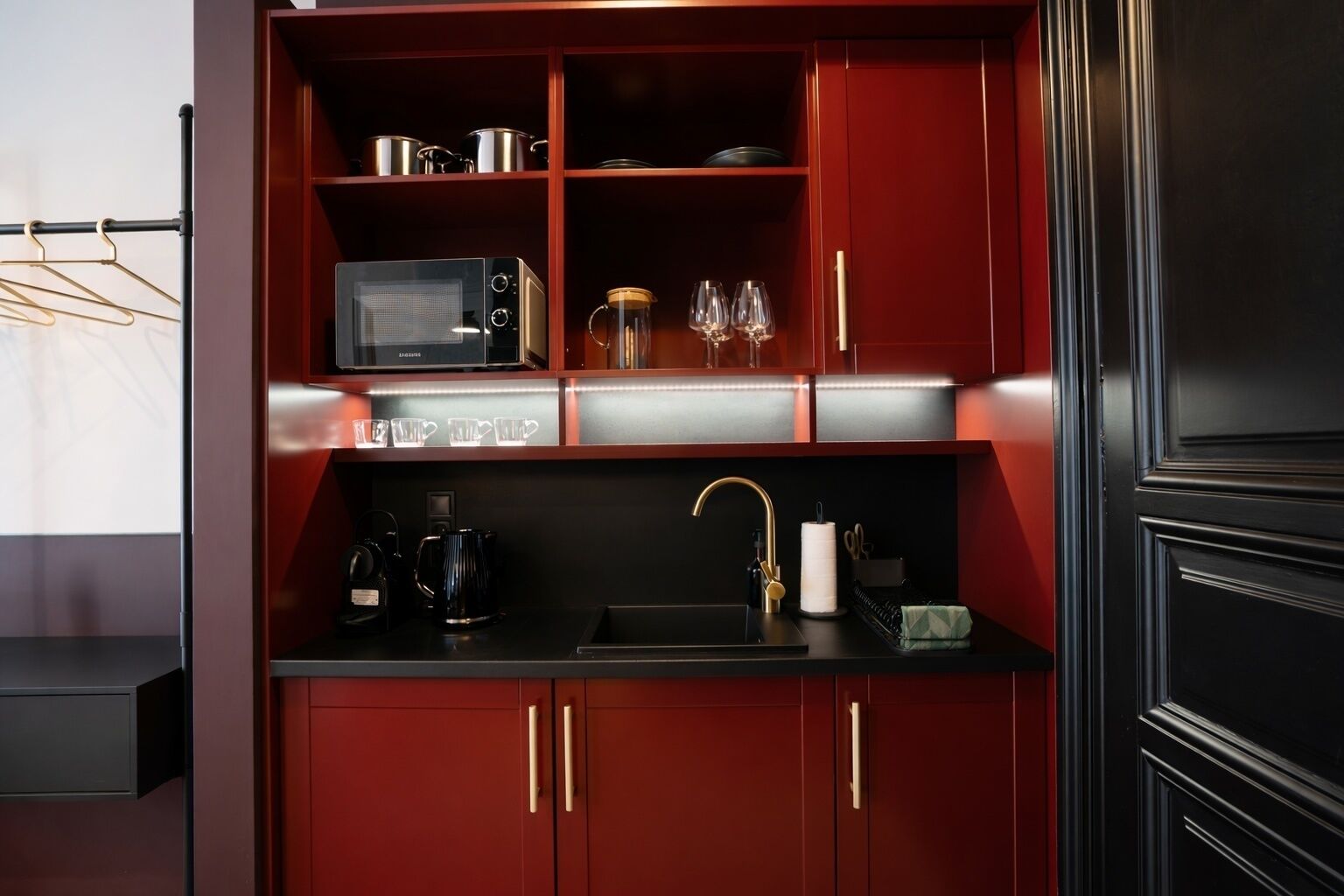 A compact kitchen with a microwave, wine glasses, and a coffee maker.