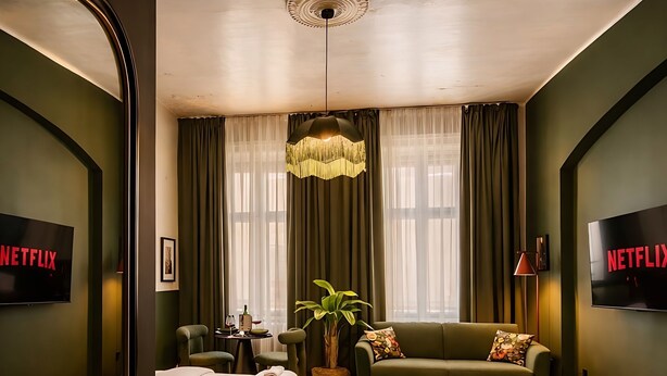 A modern hotel room with a bed, a sofa, a TV, and a large window with curtains. - Maroon & Moss Residence (Budapest)