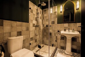 A modern bathroom with a glass-enclosed shower, a pedestal sink, and a mirror with wall sconces.