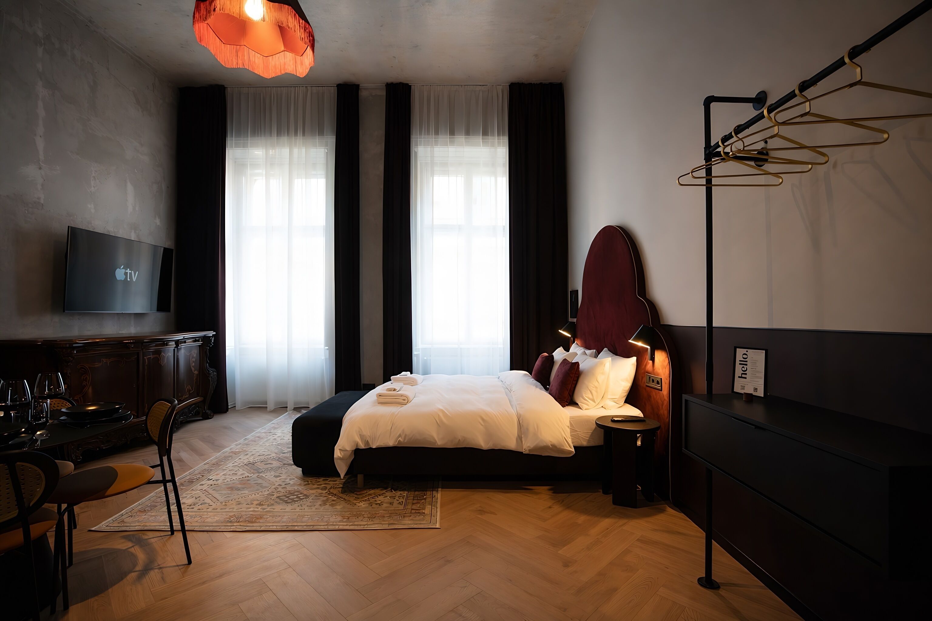 A modern hotel room with a large bed, a flat-screen TV, a desk with a chair, and a large window with curtains.