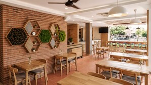 Ein Restaurant mit Ziegelwänden, sechseckigen Spiegeln, Holztischen und -stühlen, Deckenventilatoren und Blick ins Freie.