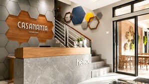 Ein Empfangsschalter mit dem Schild 'CASANANTA SEMINYA', eine Treppe und Blick auf den Außenbereich mit Sitzgelegenheiten.