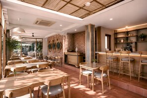 A restaurant with wooden tables and chairs, a brick wall, and a bar area. - Casananta Seminyak (Keroboken Kelod)