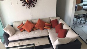 A sectional sofa with multiple cushions, a small table, and a decorative wall piece. - APARTMENT IN ACAPULCO DIAMOND ZONE (Acapulco de Juárez)