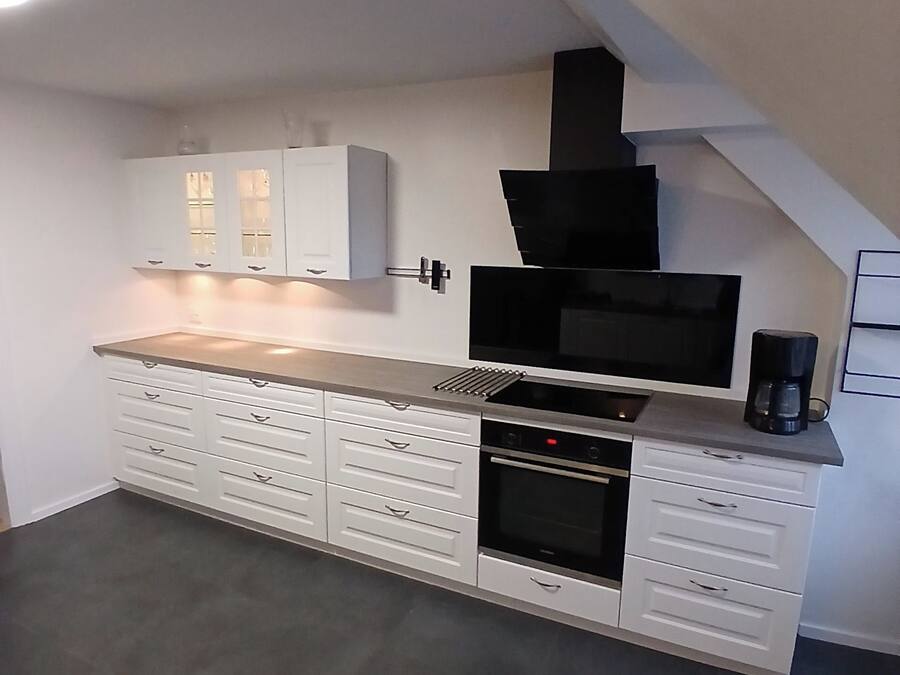 A modern kitchen with white cabinetry, a built-in oven, and a black range hood.