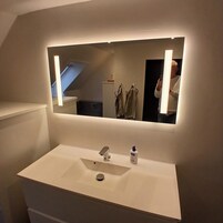 Un baño con un espejo grande, un lavamanos blanco y una botella de desinfectante para manos.