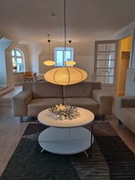 Una sala de estar moderna con un sofá grande, una mesa redonda de centro y una lámpara colgante original.