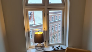 Una stanza con una finestra che si affaccia su un edificio, una lampada sul davanzale e una sedia.