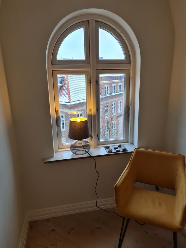 A room with a window overlooking a building, a lamp on the windowsill, and a chair. - Exclusive Apartment in center  (Frederikshavn)