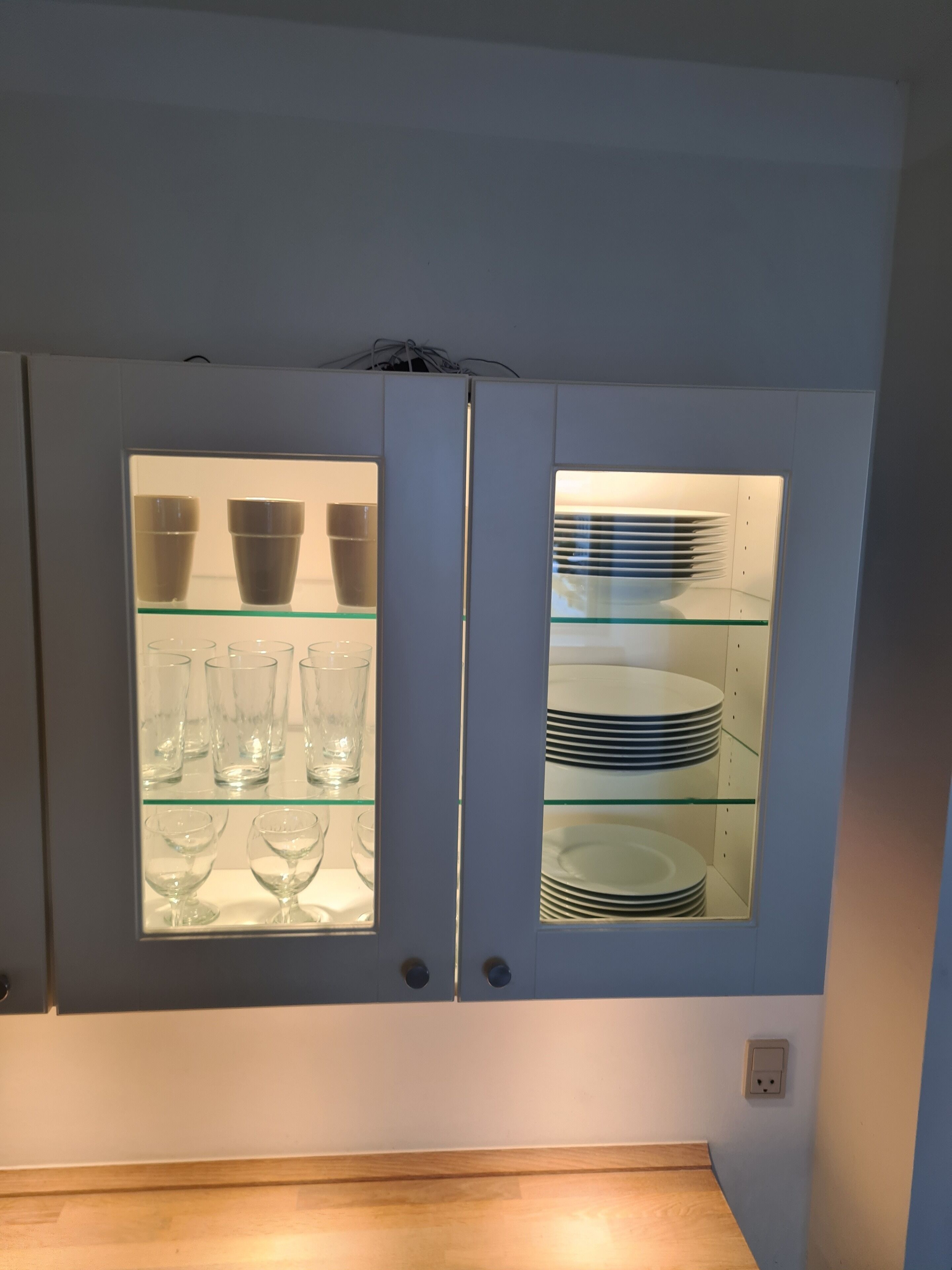 A cabinet with glass doors containing clear glassware and stacked plates.