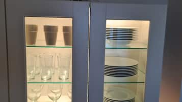 Un mobile con ante in vetro che contiene bicchieri trasparenti e piatti impilati.