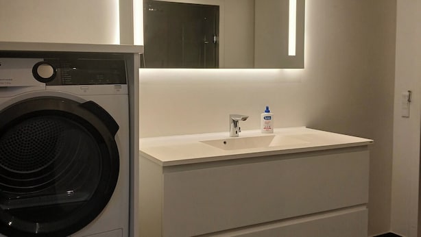 Un bagno moderno con lavatrice integrata, uno specchio grande e un mobile lavabo bianco.