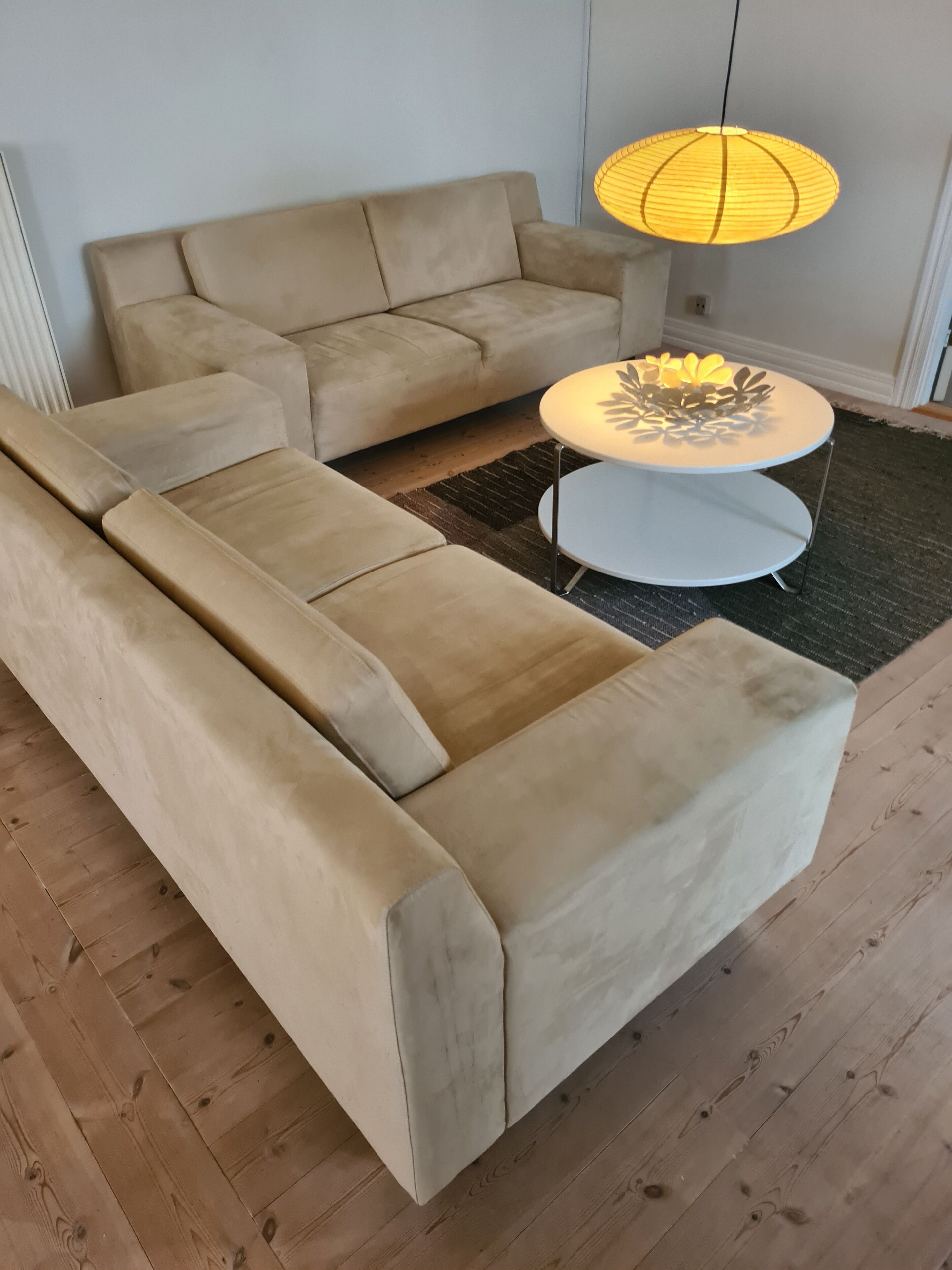 Una sala moderna con un sofá seccional color beige, una mesa de centro redonda blanca y una lámpara colgante de papel.