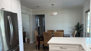 Eine moderne Küche mit weißen Schränken, einem Edelstahlkühlschrank, einem Essbereich mit Korbstühlen und einem großen Fenster.