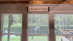 A wooden ceiling with exposed beams and a sign that reads "a thankful heart" above three windows with blinds.