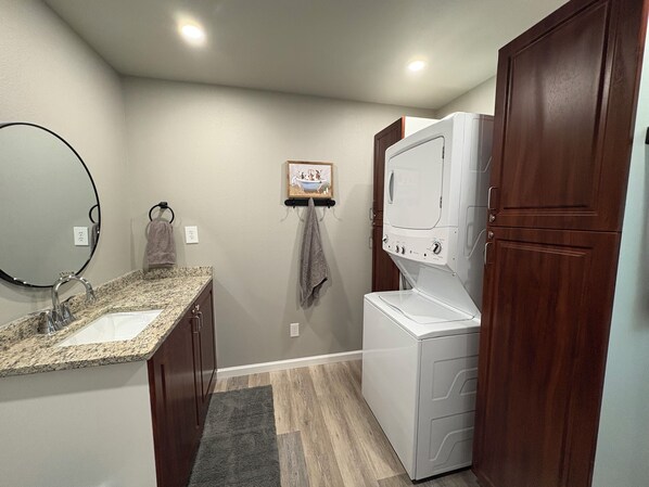 A compact laundry room with a washing machine, a sink, and a mirror.