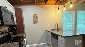 A modern kitchen with granite countertops, stainless steel appliances, and a wooden ceiling.
