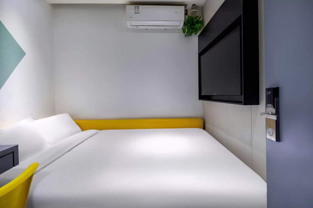 Une chambre d’hôtel moderne équipée d’un lit, d’un téléviseur fixé au mur et d’un appareil de climatisation placé au-dessus du lit.