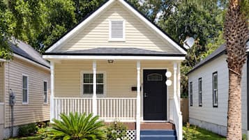 A single-story house with a front porch, a black door, and a small front yard with a palm tree.