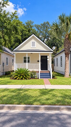 A single-story house with a front porch, a black door, and a small front yard with a palm tree. - Cozy 2BR Downtown Retreat Just 5 Min to UF Health (Jacksonville)