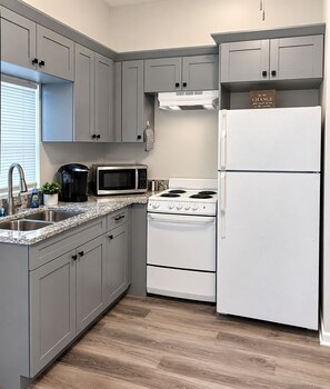 A kitchen with grey cabinets, a white stove, a white refrigerator, and a microwave. - Cozy 2BR Downtown Retreat Just 5 Min to UF Health (Jacksonville)