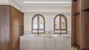 A modern kitchen with two arched windows, white cabinetry, and a central island. - 3-bedroom house in good condition with cool AC (Woodmere)